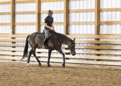 A person riding a dark horse indoors with a helmet and casual gear.