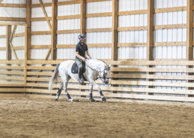 A rider on a white horse inside an indoor riding arena.