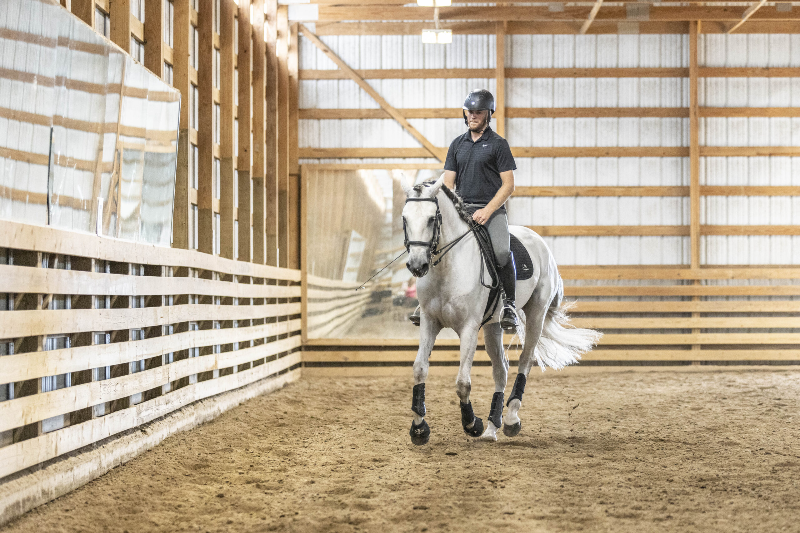 Person riding a white horse in an indoor arena.