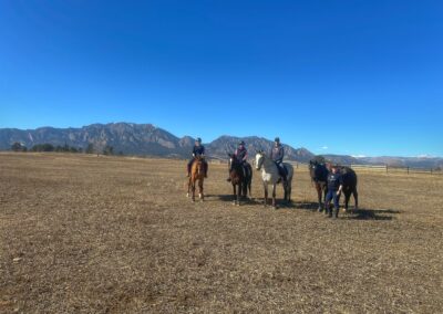 Four people riding horses on a dry field under a clear blue sky.