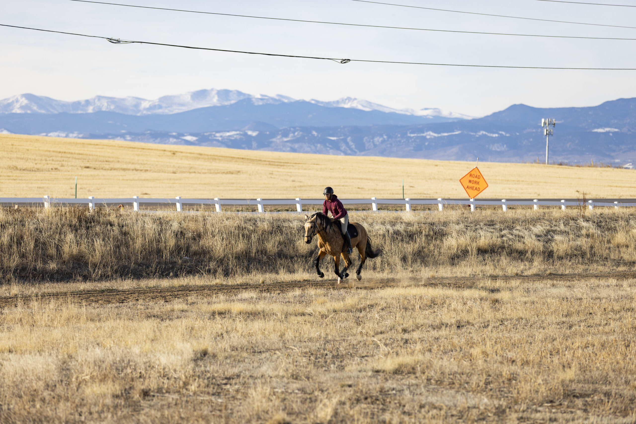 Rider on horseback galloping across dry grassland with mountains in the background.